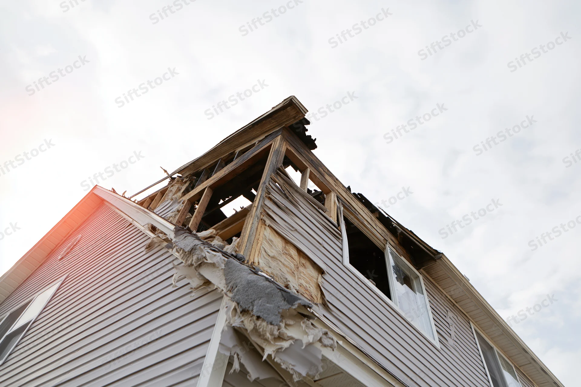 Fire-damaged two-story house with collapsed roof and exposed framing under overcast sky