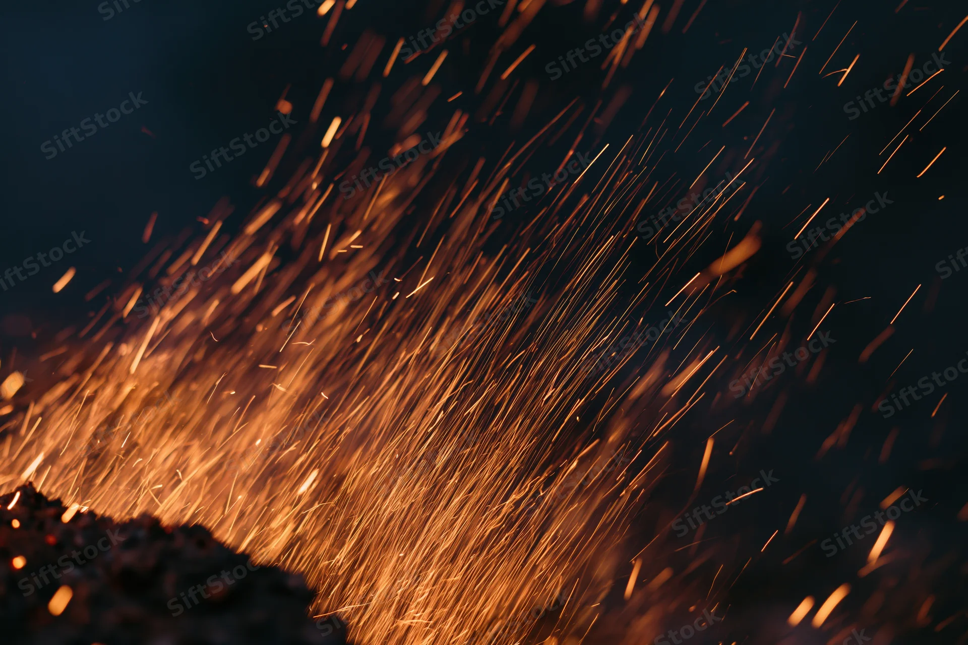 Glowing sparks flying upward from a dark surface at night