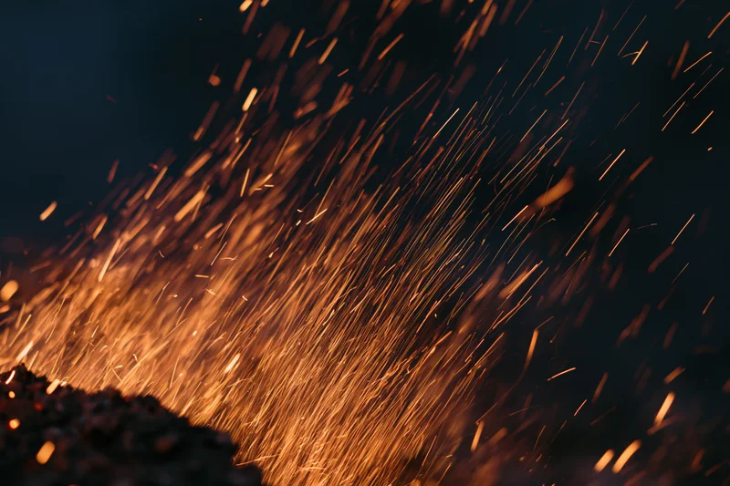 Glowing sparks flying upward from a dark surface at night