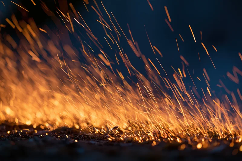 Glowing sparks flying upward from a dark surface at night