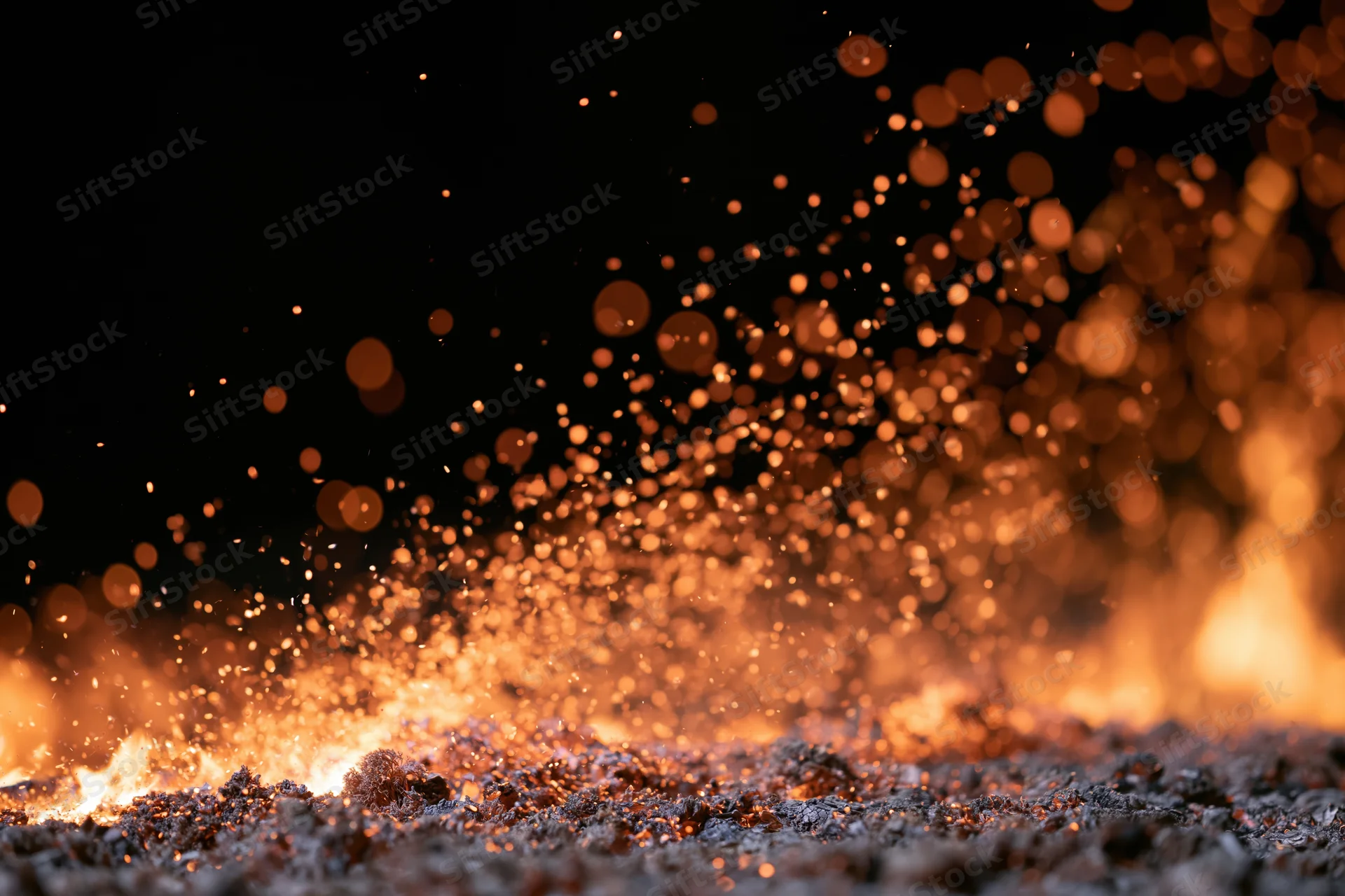 Fire embers and sparks rising from burning flames on dark ground