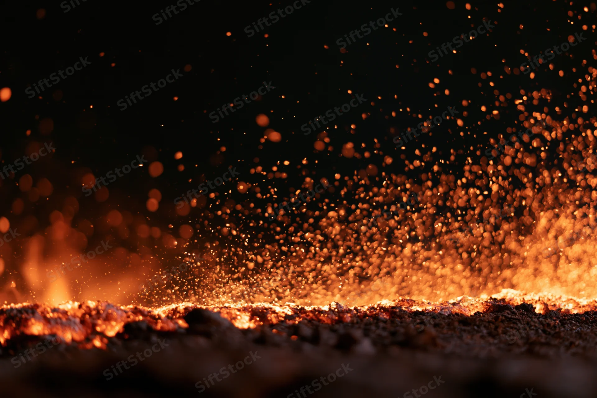 Fire embers and sparks exploding upward from open flames at night