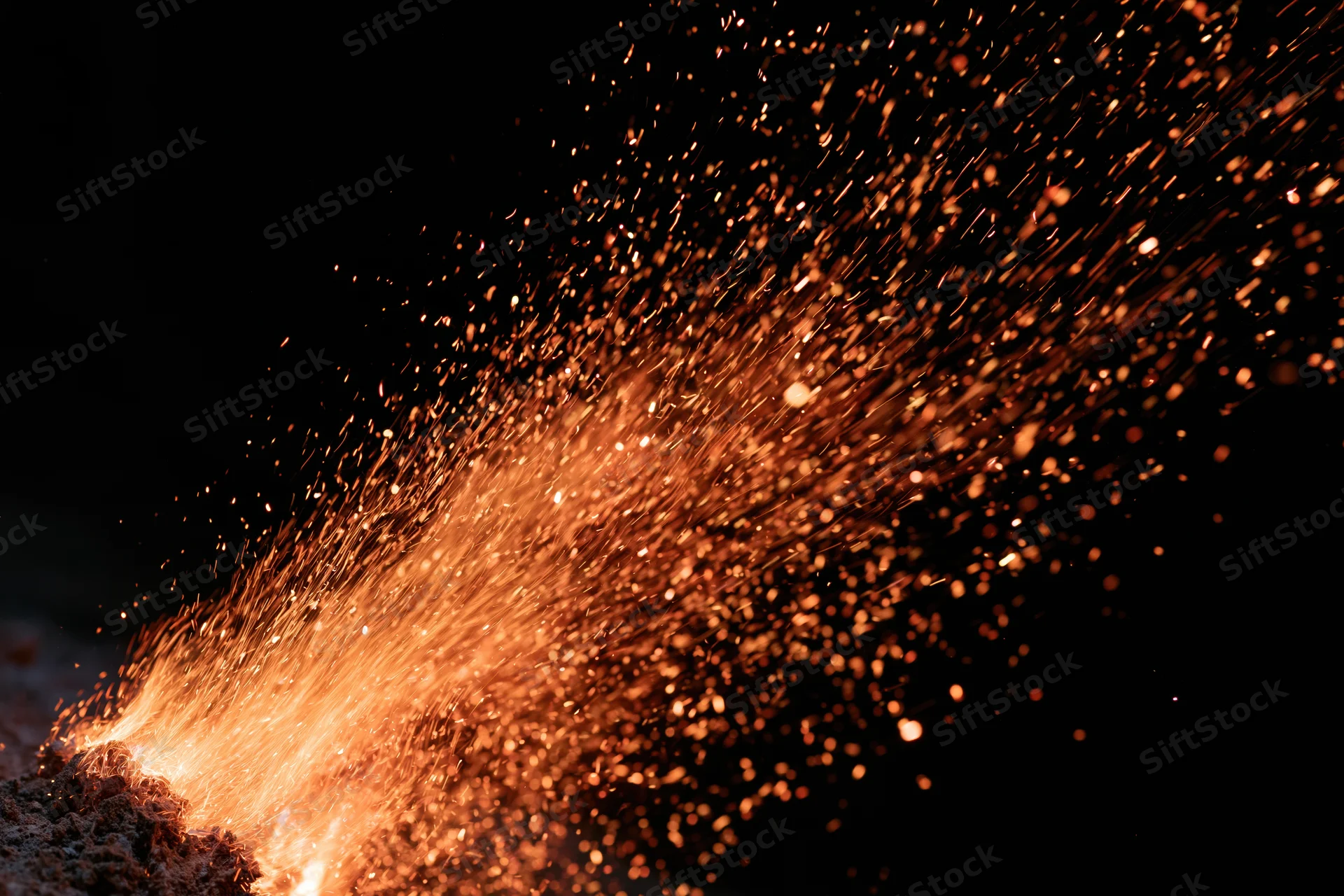 Fiery sparks bursting upward from a glowing source against a dark background