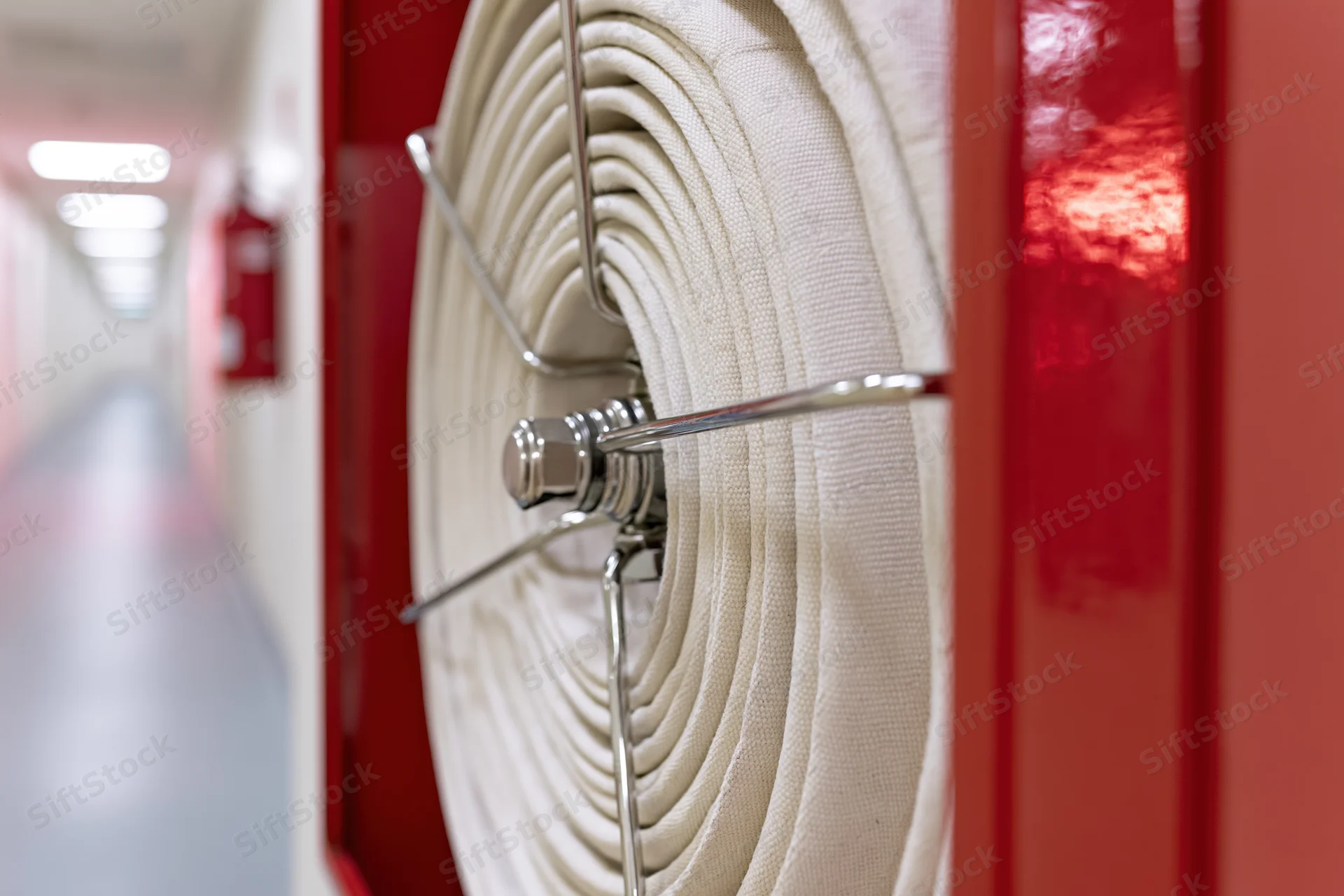 Coiled fire hose on a reel mounted in an open red wall cabinet in a hallway