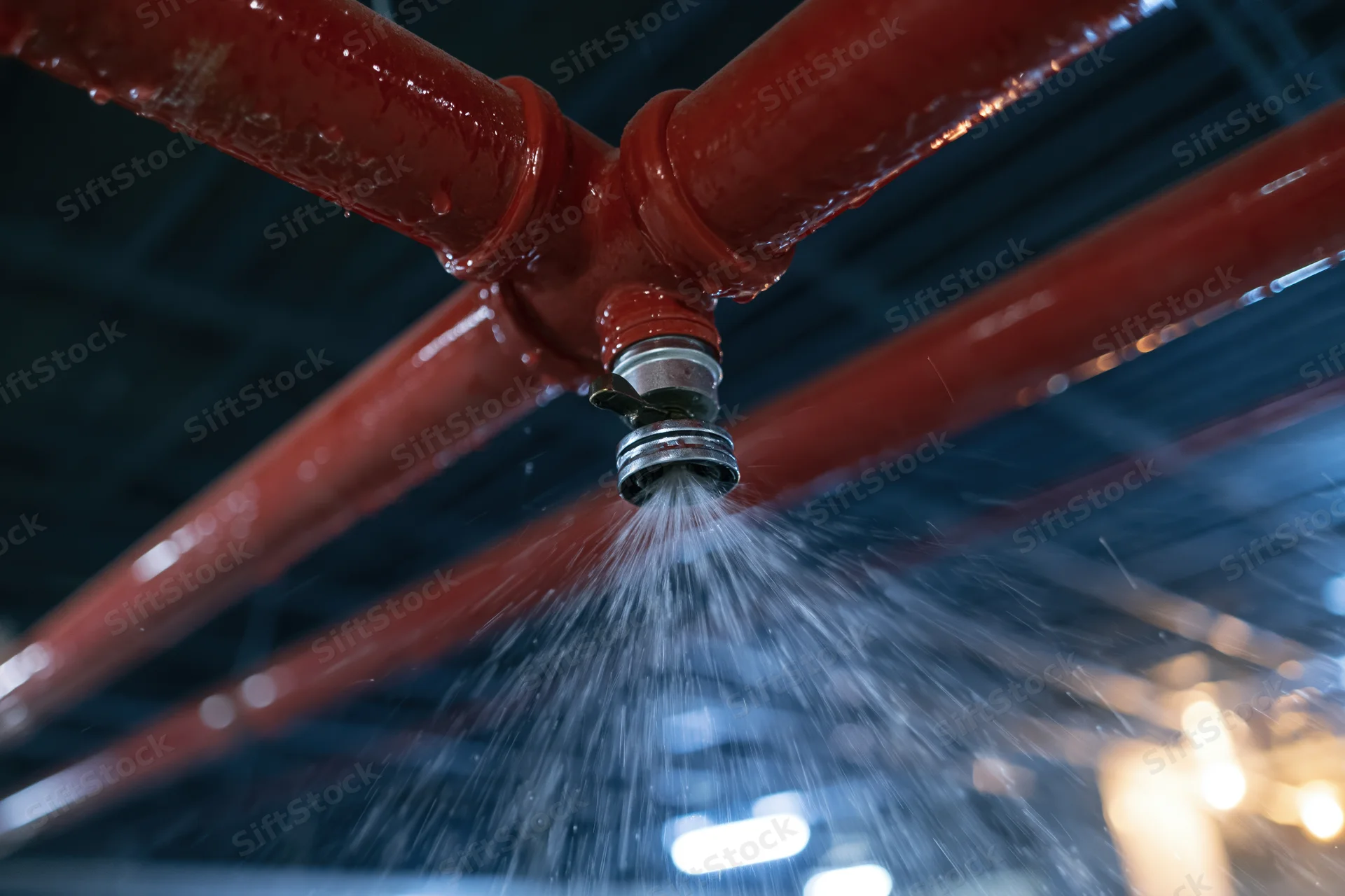 Fire suppression sprinkler head discharging water from ceiling pipes in industrial building interior