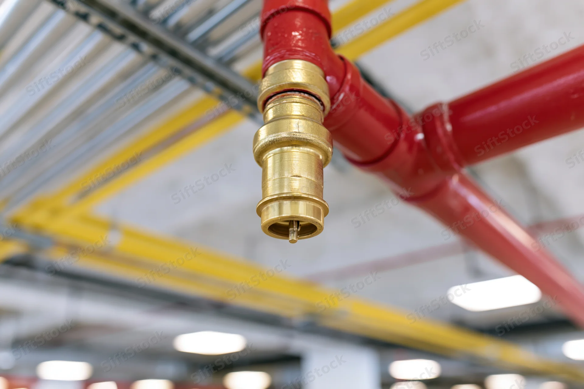 Fire suppression sprinkler head mounted on red steel pipe under industrial ceiling