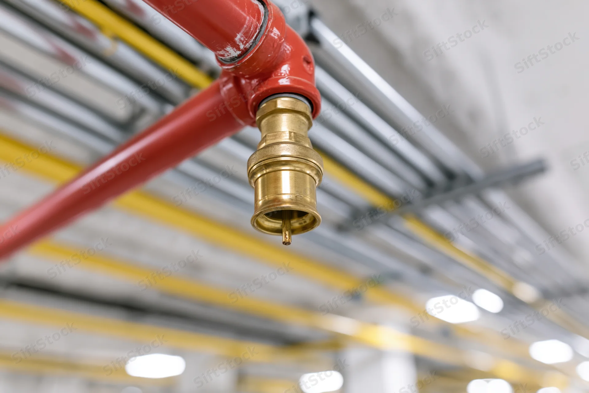 Fire suppression sprinkler head mounted on red steel pipe in industrial ceiling