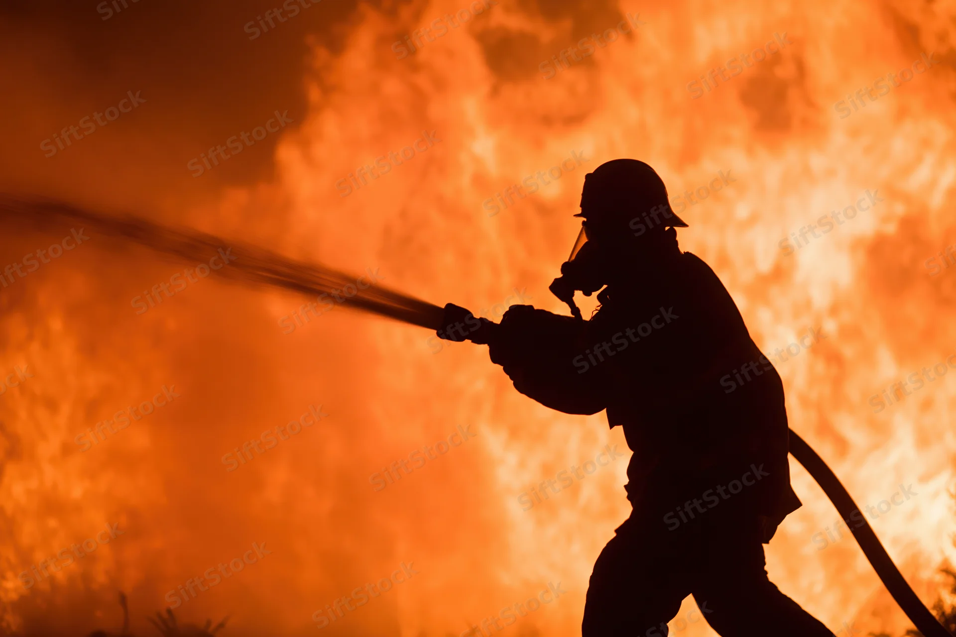 Firefighter spraying water from a hose against a wall of flames
