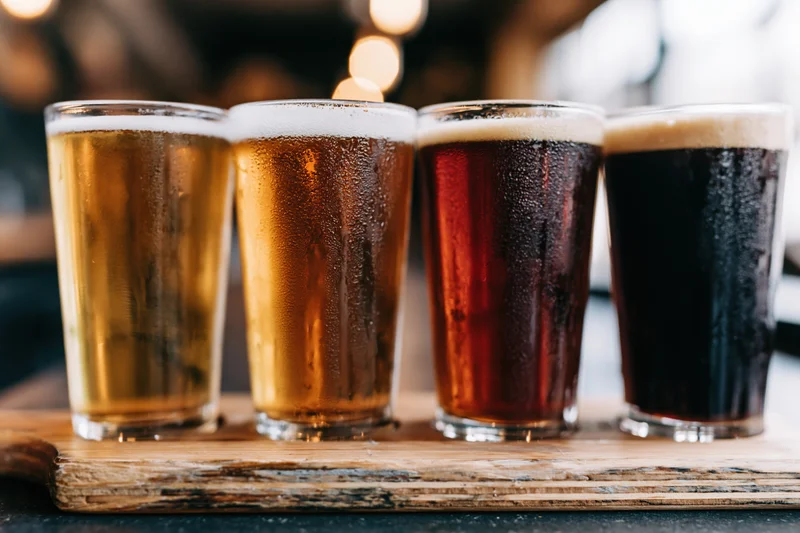 Four craft beer tasting glasses in a row on a wooden board with condensation and foam
