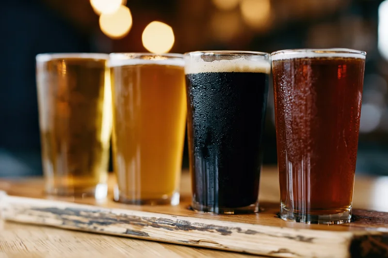 Four craft beer tasting glasses in a row on a wooden tray at a bar