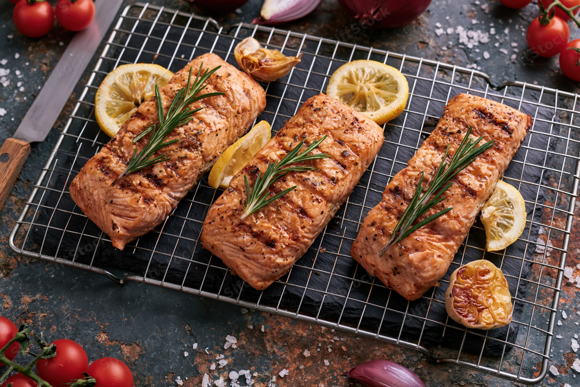 Grilled salmon fillets arranged on a wire rack with lemon slices and rosemary sprigs on a dark slate board