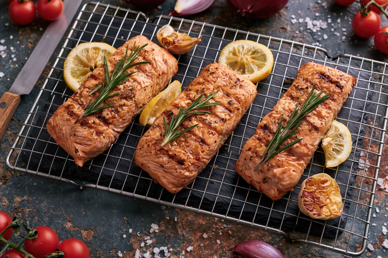 Grilled salmon fillets arranged on a wire rack with lemon slices and rosemary sprigs on a dark slate board