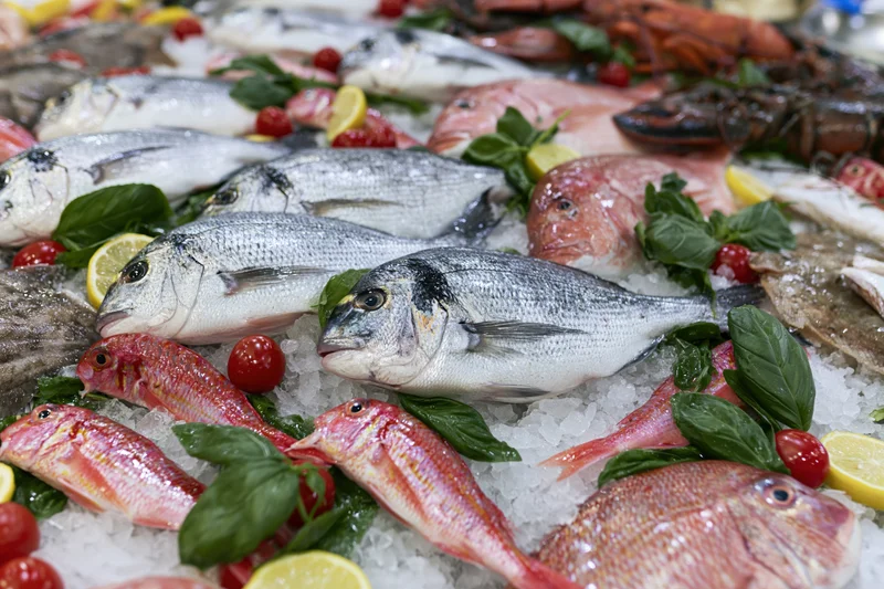 Whole fresh fish and shellfish arranged on crushed ice with herbs and citrus for market display