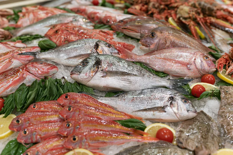 Fresh whole fish and shellfish densely arranged on crushed ice with herbs and citrus at a seafood market display