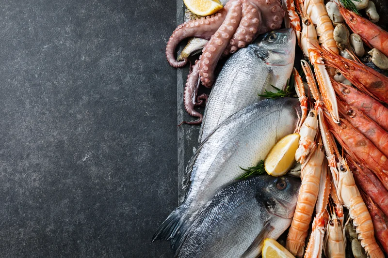 Fresh whole fish octopus and langoustines arranged on dark slate with lemon and rosemary garnish