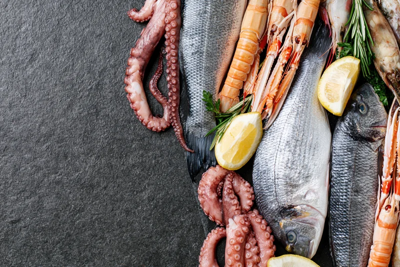 Fresh whole fish octopus and langoustines arranged on a black slate surface with lemon and rosemary garnish