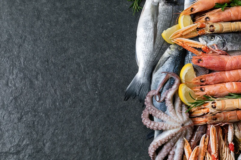 Fresh whole fish octopus langoustines and mixed seafood arranged on dark slate surface with lemon and herbs
