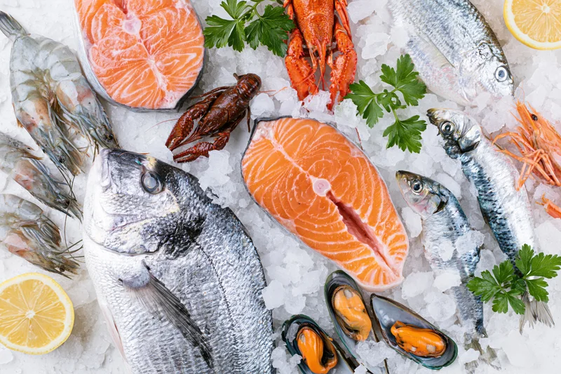 Fresh seafood including whole sea bream, salmon steaks, prawns, crawfish and mussels arranged on ice with lemon and parsley