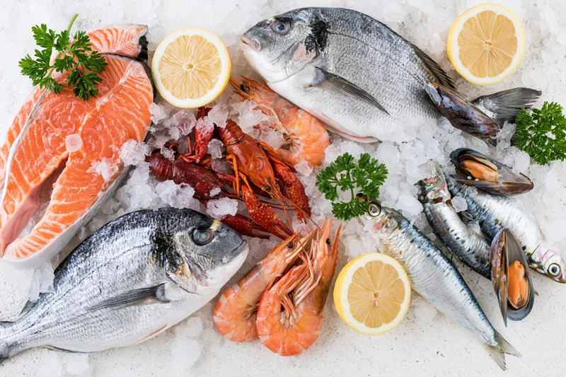 Fresh whole fish and shellfish arranged on ice with lemon and parsley for display