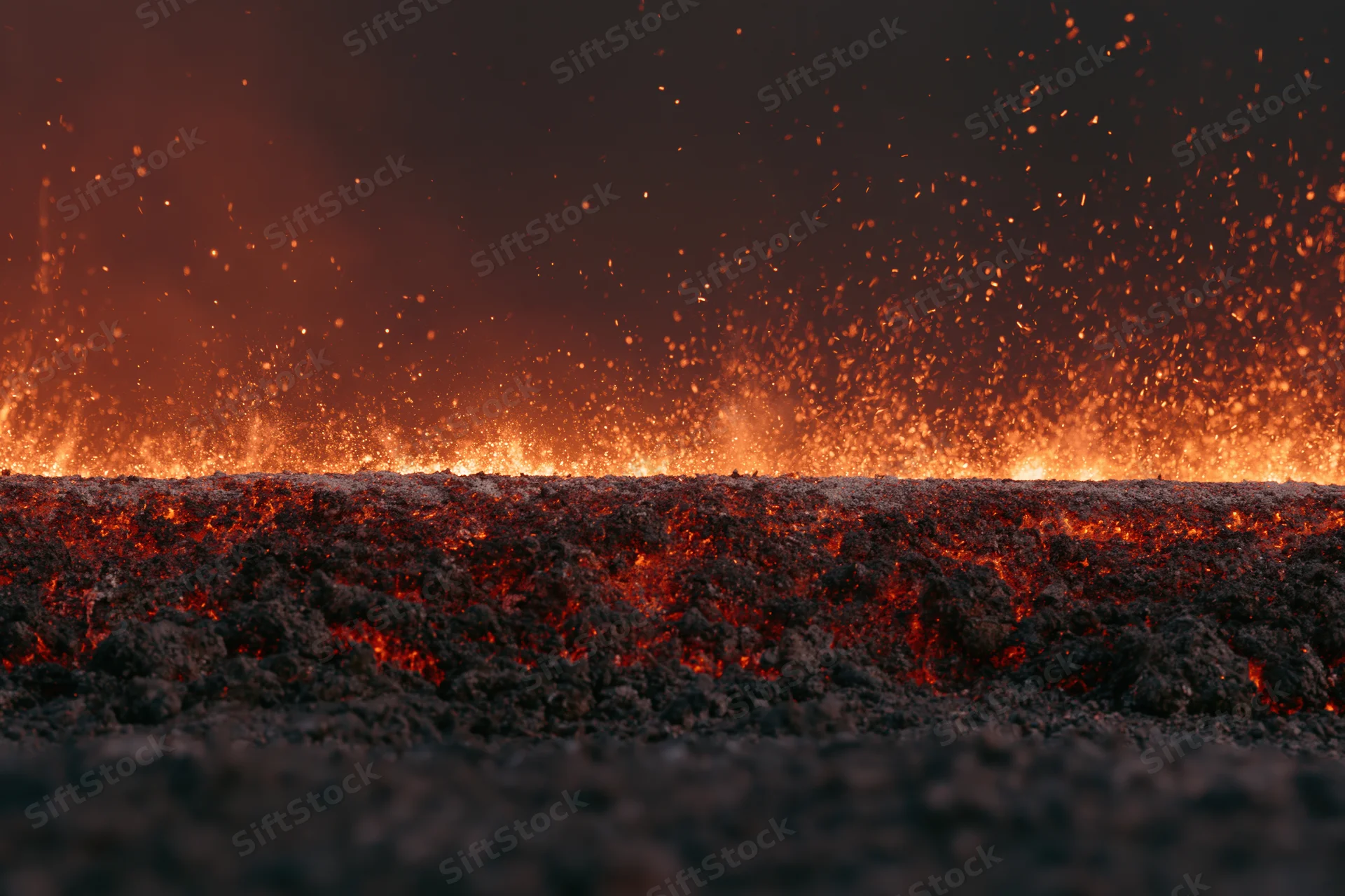 Glowing coal embers burning along the ground at night with sparks rising into the dark sky