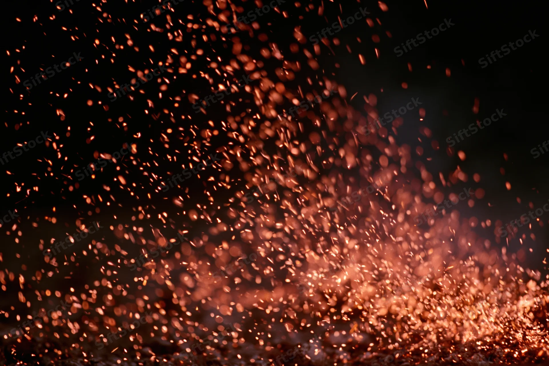 Glowing orange and red sparks flying upward against a dark background