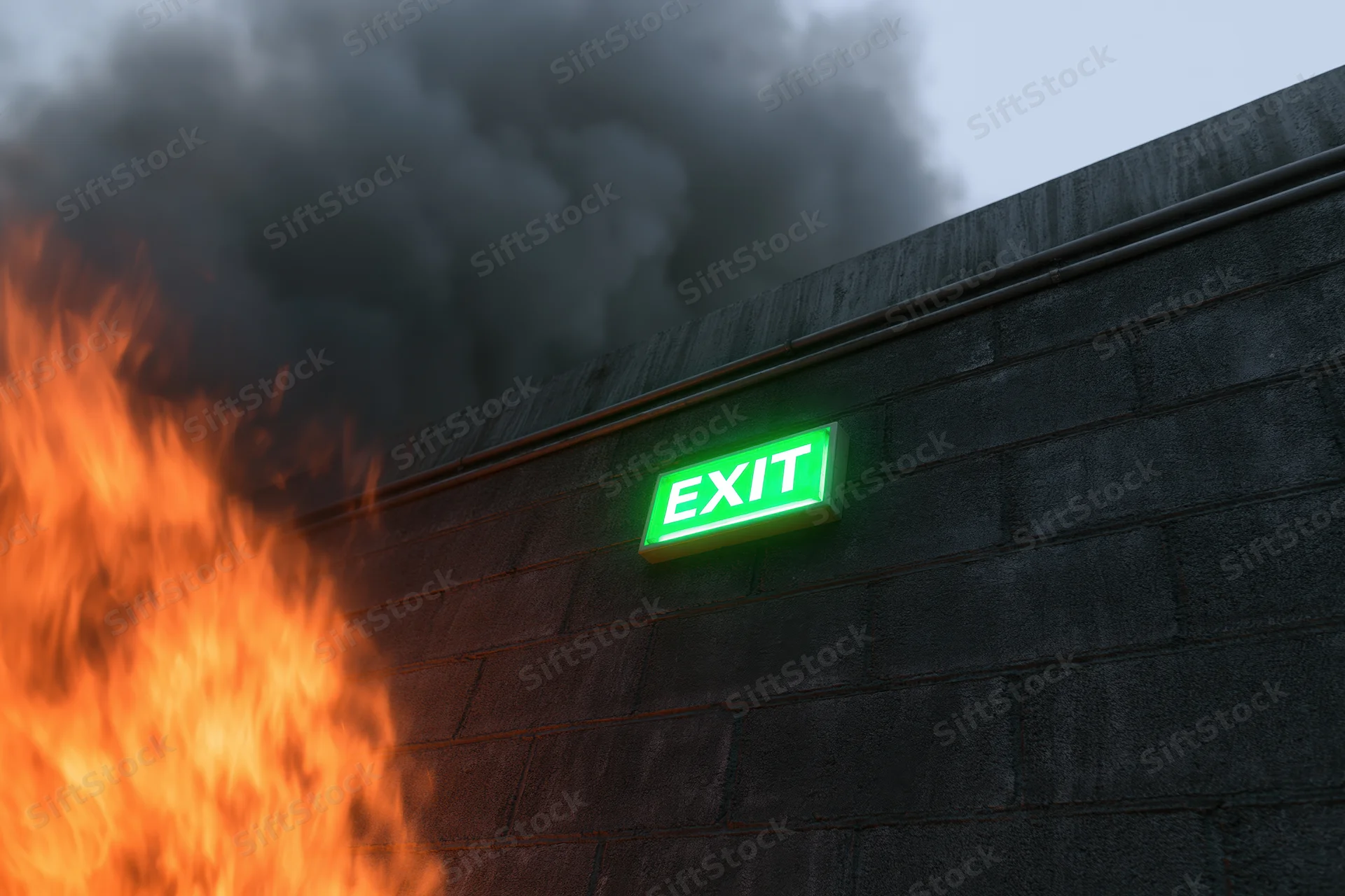 Green illuminated exit sign on concrete wall with flames and smoke nearby