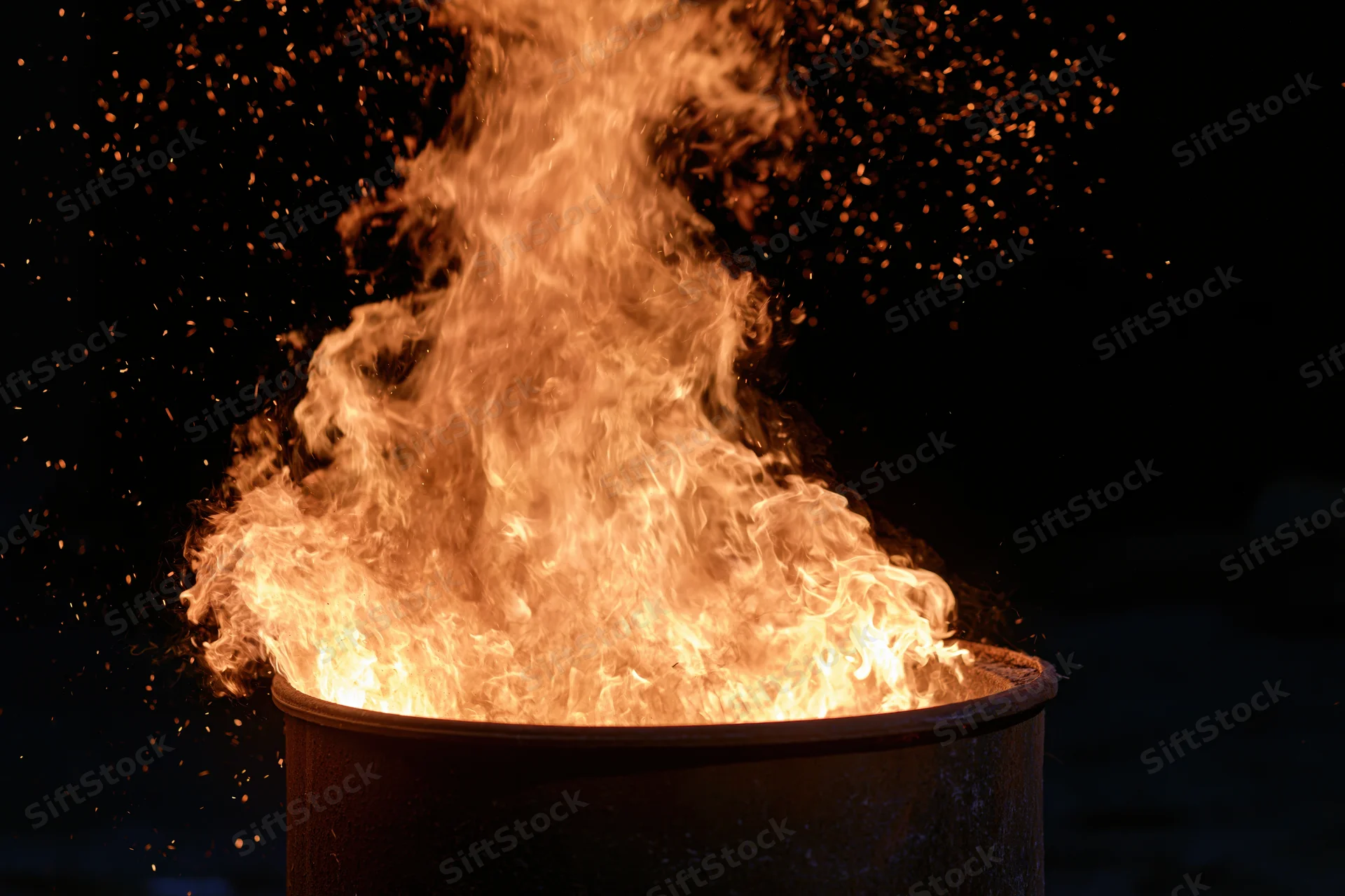 Intense flames and sparks erupting from a metal barrel at night