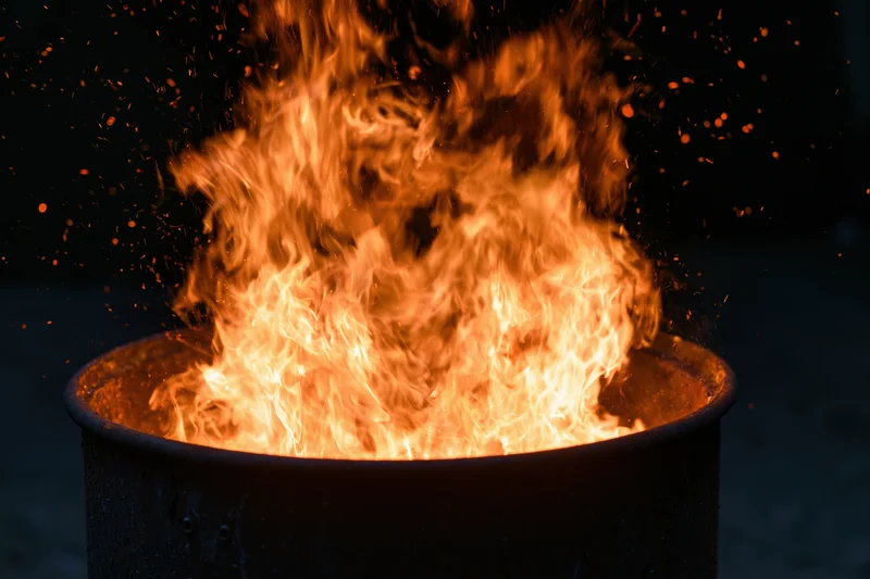 Intense fire burning inside a metal barrel at night