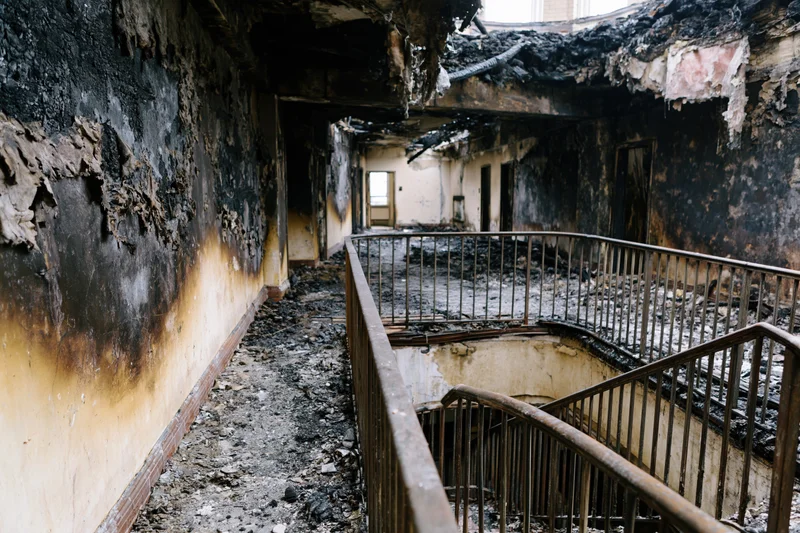 Charred interior of abandoned building with collapsed ceiling and debris-covered floors and stairwell