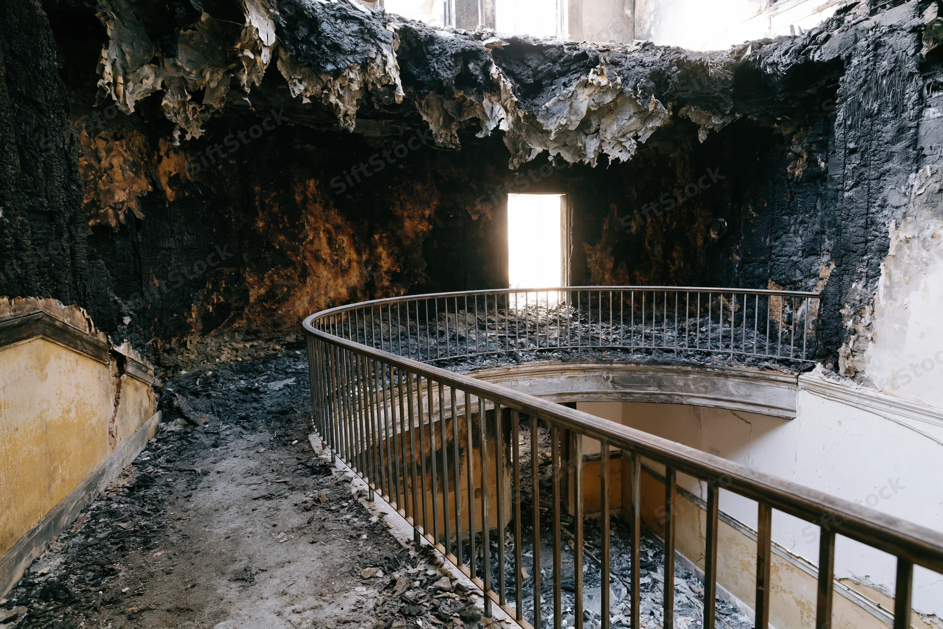 Charred interior of abandoned building with spiral staircase and rubble under daylight