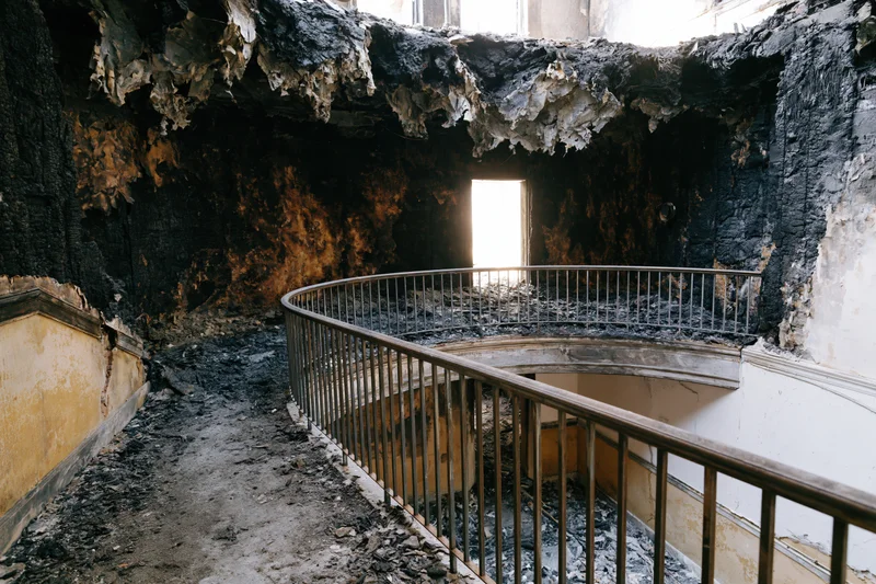 Charred interior of abandoned building with spiral staircase and rubble under daylight