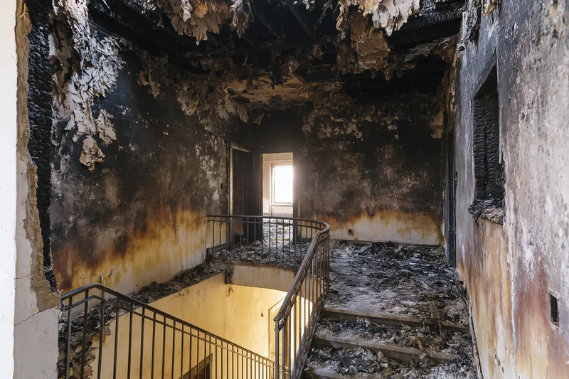Charred interior of abandoned building with damaged stairs and railing, showing fire damage and debris