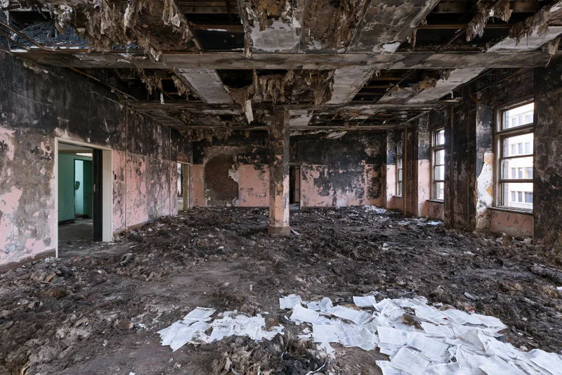 Fire-damaged interior of abandoned building with charred walls and debris on floor