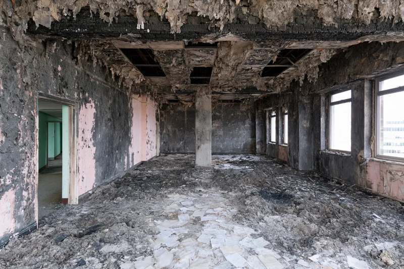 Fire-damaged interior of an abandoned building with charred walls and debris on the floor