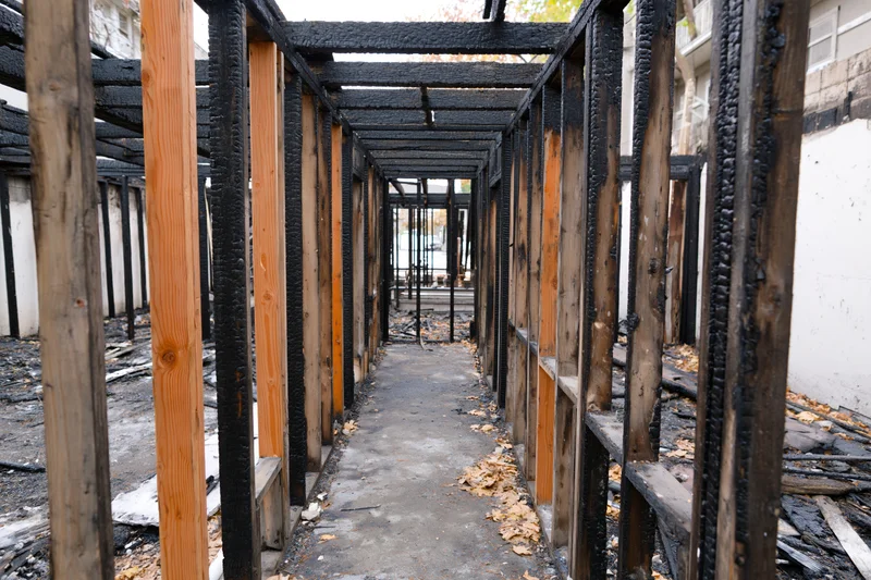 Charred wooden frame of a fire-damaged building interior with exposed beams and debris on the floor