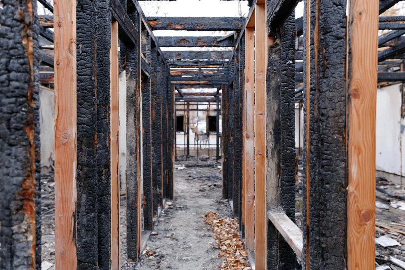 Charred wooden frame of a fire-damaged building interior with debris on floor
