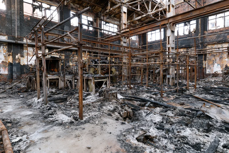 Burned industrial factory interior with charred metal framework and rubble on concrete floor