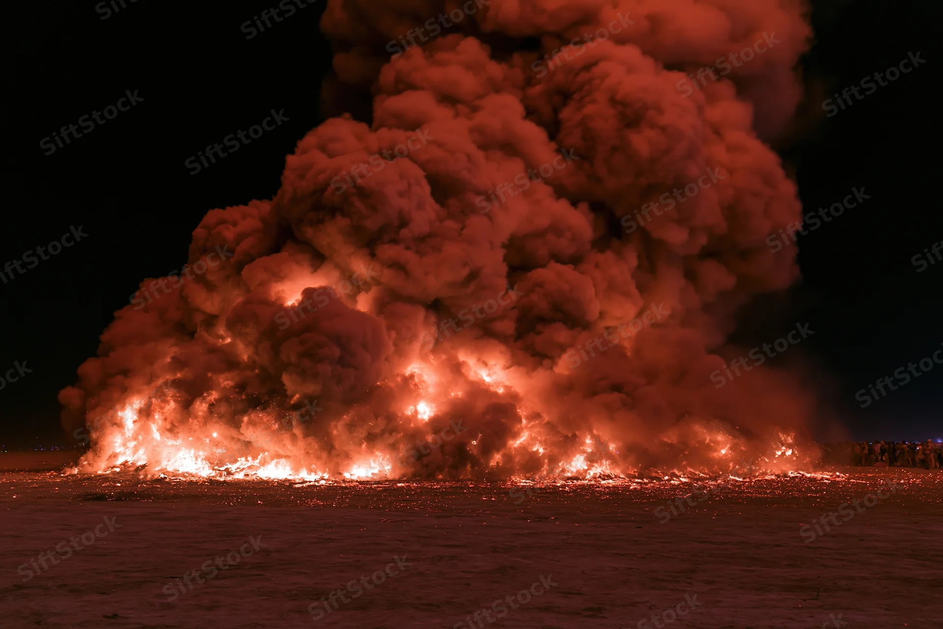 Large effigy structure engulfed in flames collapsing at night on snowy ground