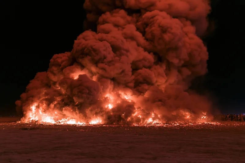 Large effigy structure engulfed in flames collapsing at night on snowy ground