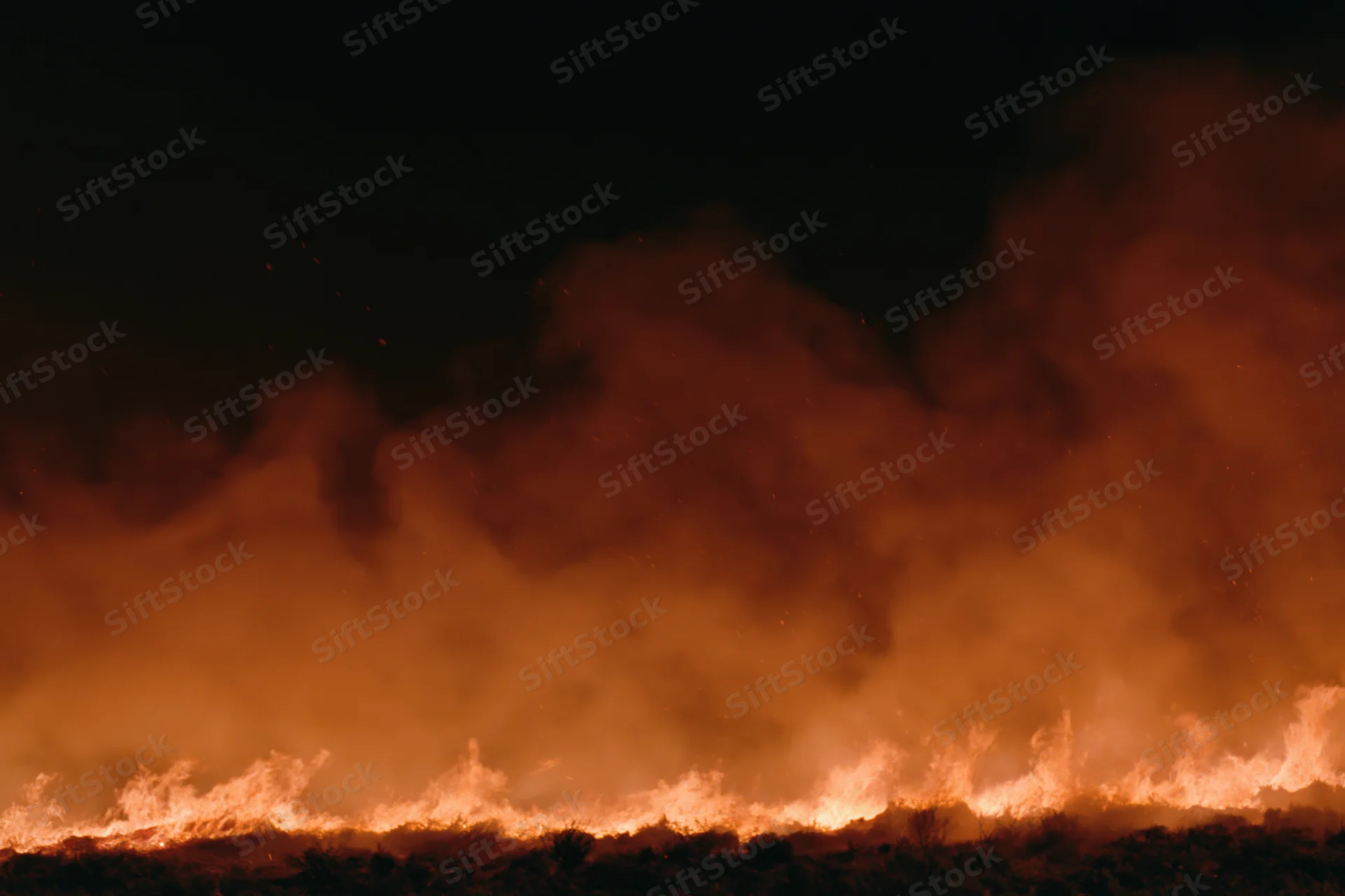 Flames burning across a dark landscape at night with thick smoke rising