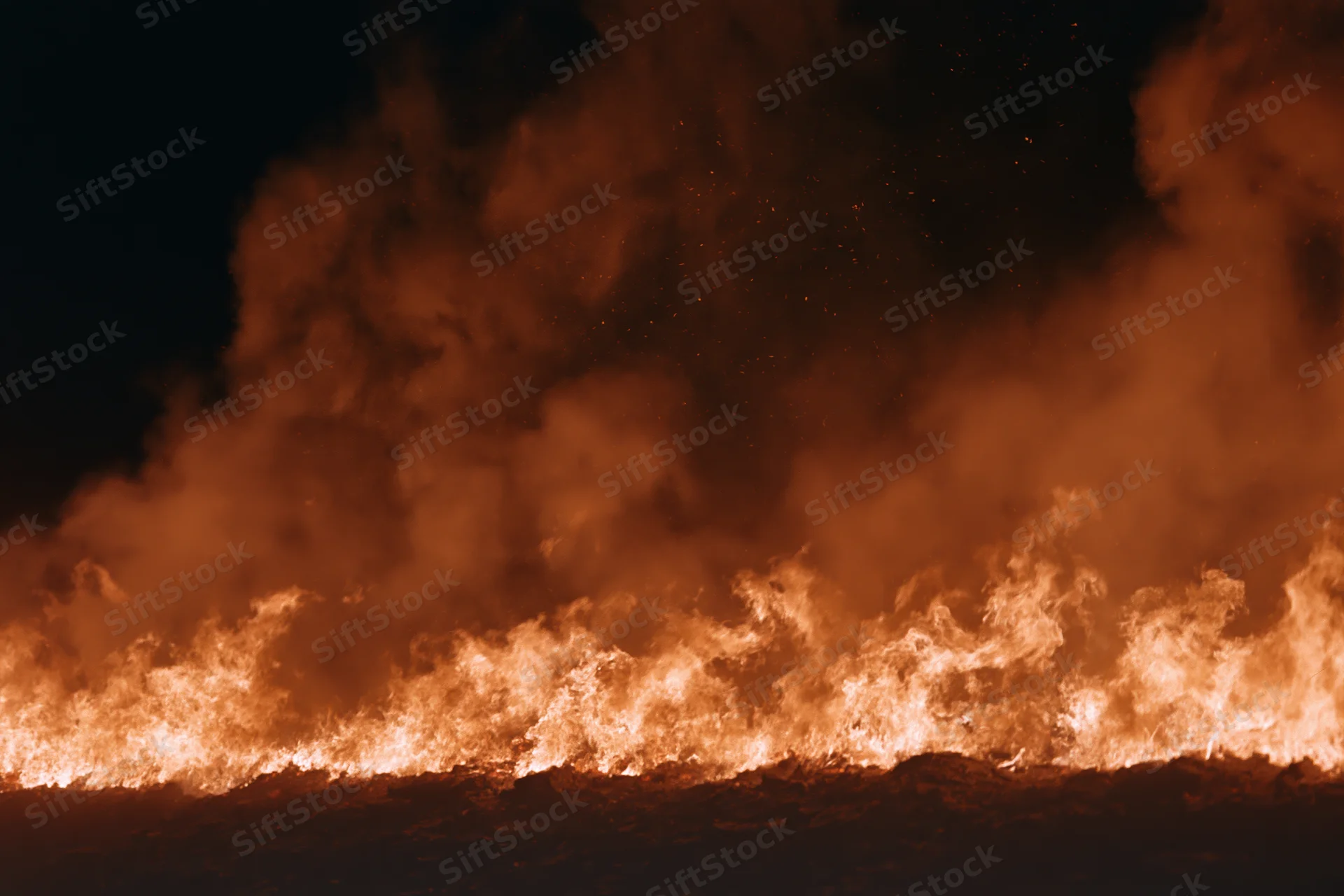 Large fire burning along the ground at night with flames and smoke rising