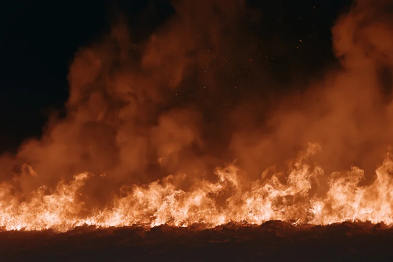 Large fire burning along the ground at night with flames and smoke rising