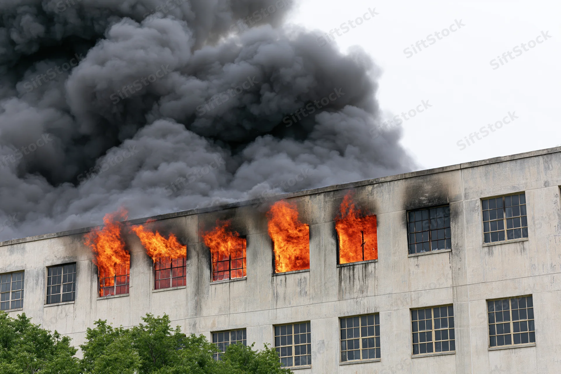 Flames erupting from windows of a large industrial concrete building during a fire emergency