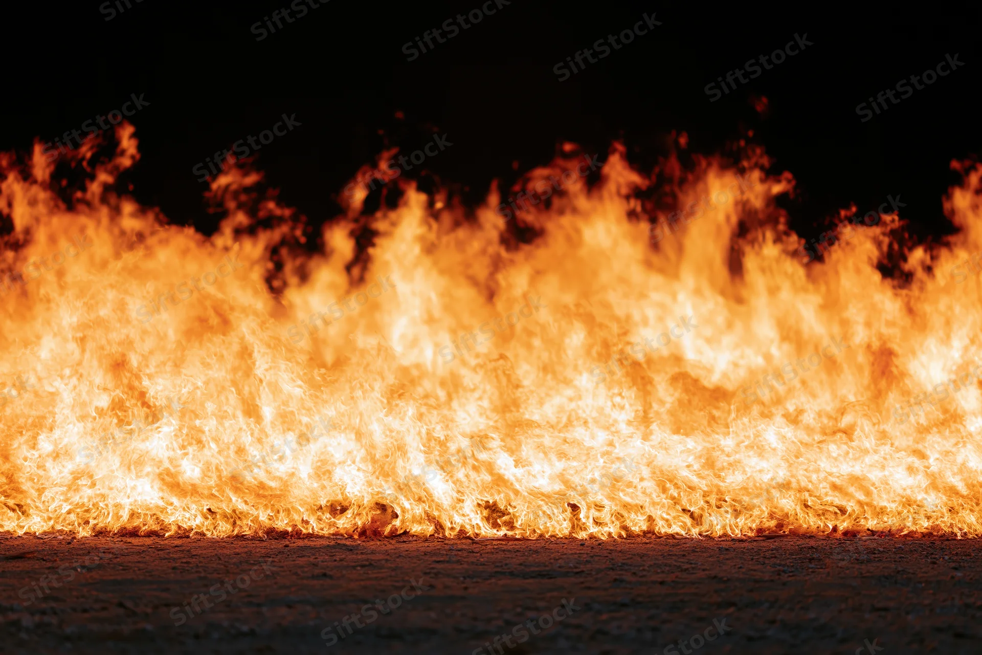 Intense industrial fire burning at ground level on dark pavement