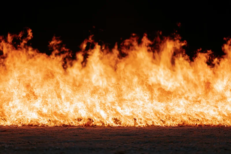Intense industrial fire burning at ground level on dark pavement