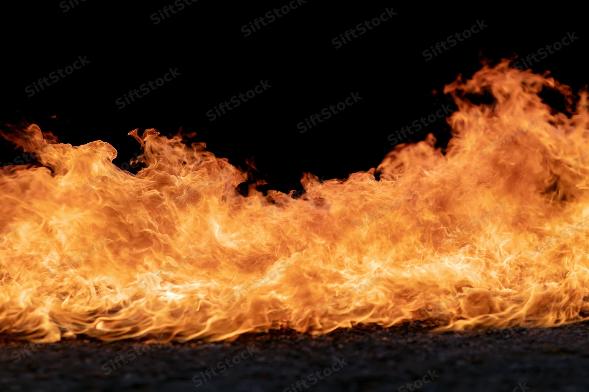Intense flames burning across dark asphalt surface against black background