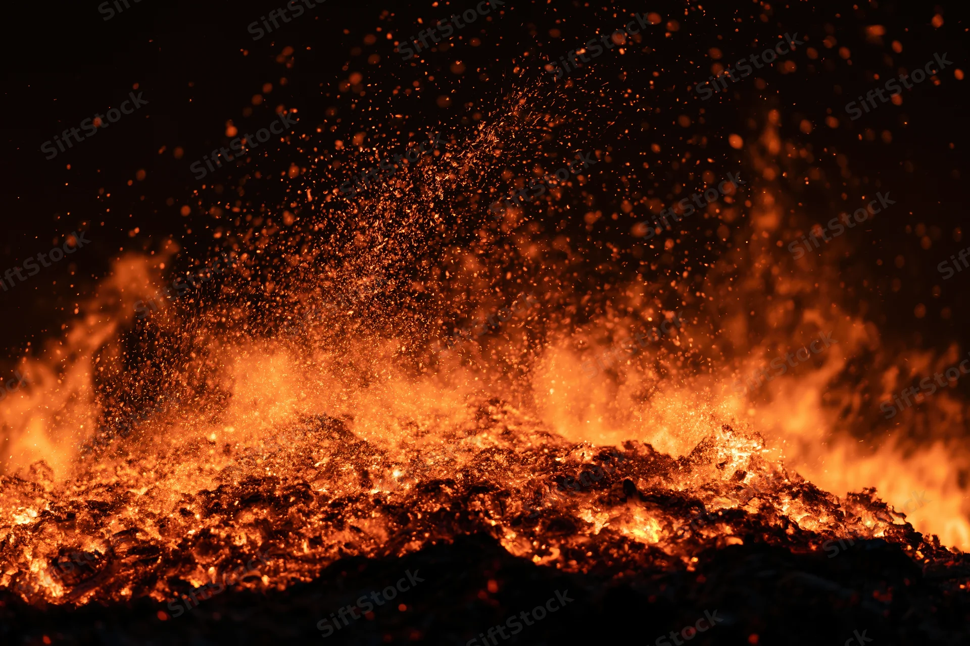 Intense fire burning at night with glowing embers and sparks flying upward