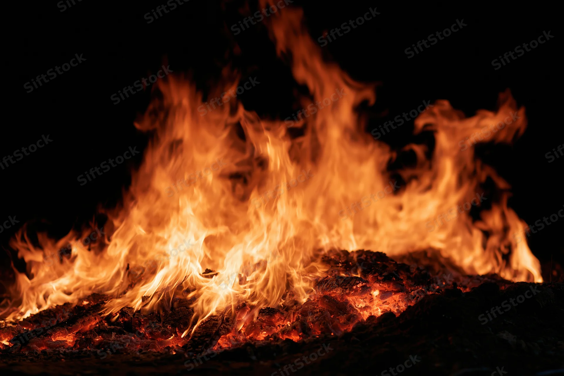 Intense flames burning over glowing embers at night