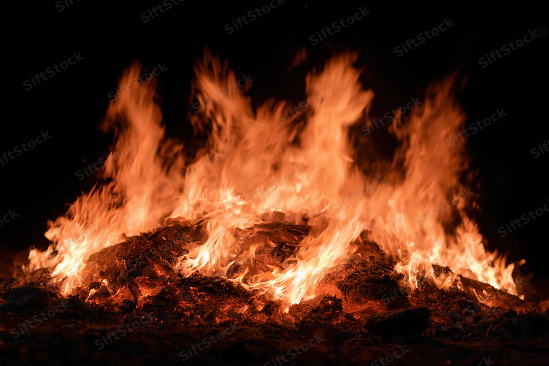 Intense flames burning brightly at night over charred logs in a dark outdoor setting