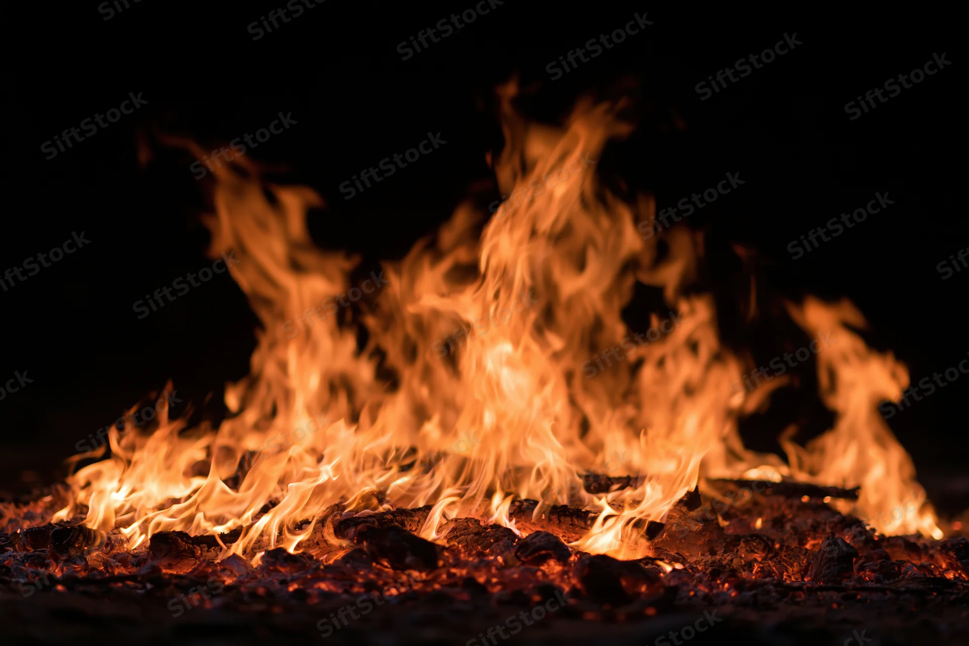 Intense flames burning over glowing embers at night